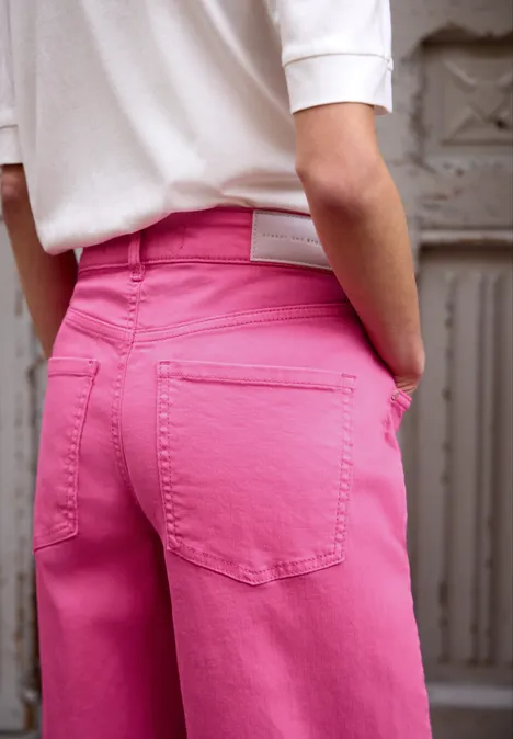 Barrel Leg Jeans im Loose Fit pink washed Nahaufnahme einer Person von hinten, trägt ein weißes Top und knallpinke Hose, steht vor einer grauen Metalltür.