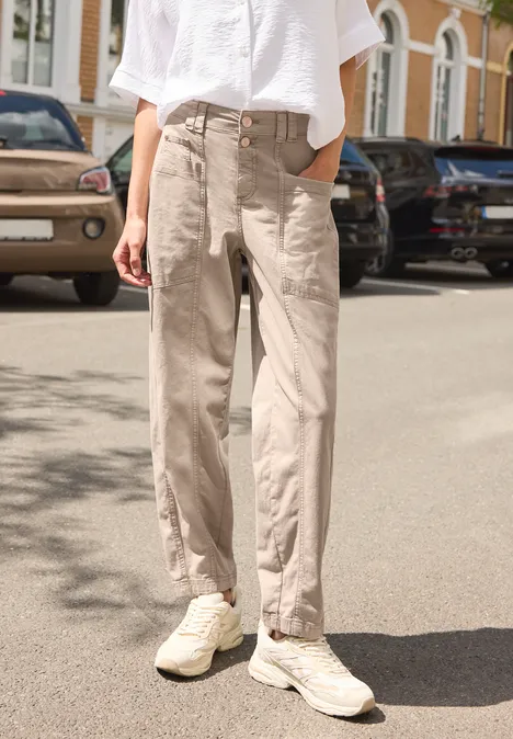 Personne debout dans la rue, chemise blanche, pantalon beige ample et baskets blanches.