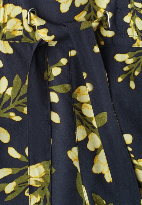 Robe bleu foncé à imprimé floral jaune et blanc avec feuillage vert et ceinture nouée.