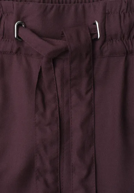 Close-up van een bordeauxrode tailleband met geïntegreerde stoffen riem en zilverkleurige oogjes