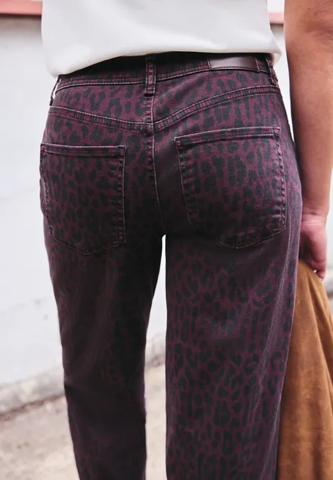 High Waist Barrel Leg Jeans mit Leo-Print burgundi printed wash Nahaufnahme einer Person von hinten in hoch taillierten, lila Leoparden-Jeans, dazu weißes Oberteil und braune Tasche.
