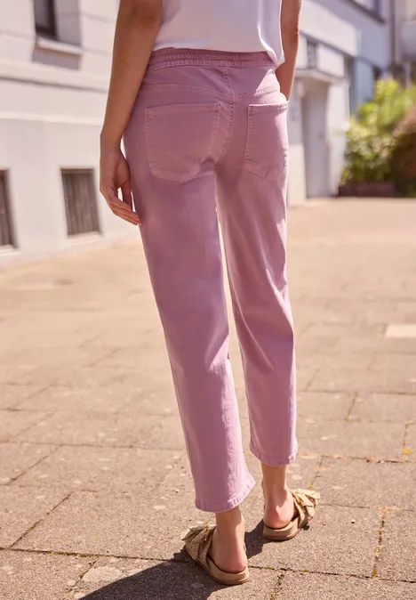 Frau von hinten in rosa Hose und Sandalen läuft auf sonnigem Gehweg.
