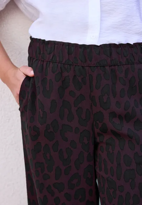 Pantalon à motif léopard noir, taille élastique et main dans la poche, associé à un chemisier blanc