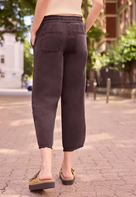 Achteraanzicht van persoon in zwarte, knielange broek en sandalen op een geplaveide straat.