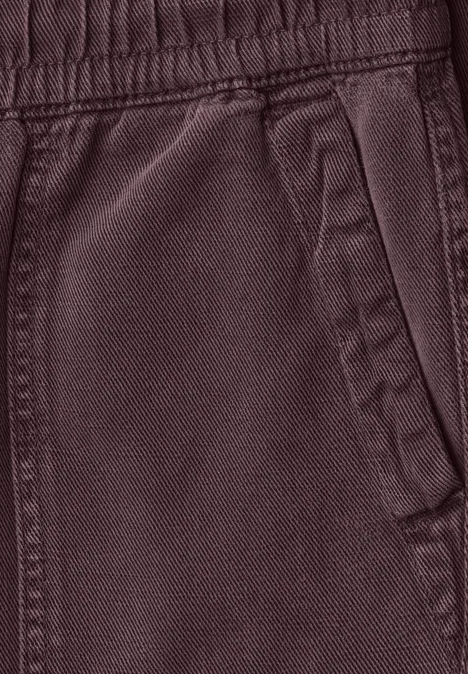 Close-up van een donkerrode joggingbroek met elastische tailleband en zijzak.