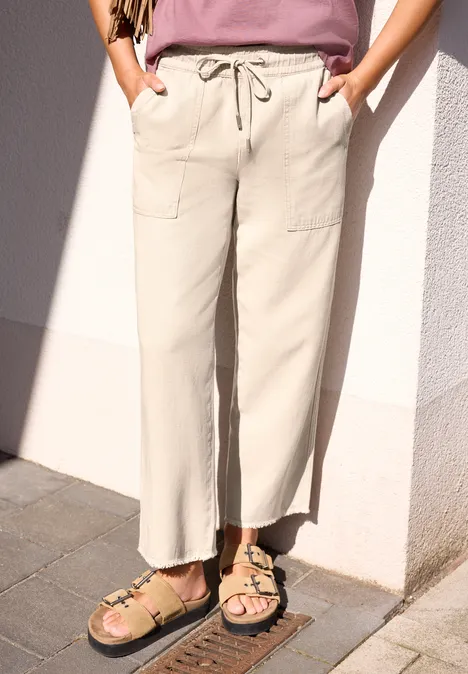 Broek met Mid Waist-taille en Straight Leg-pijpen in een Loose Fit-pasvorm dark creamed sand Vrouw in beige, wijde broek met koord en zakken, sandalen aan, voor een witte muur.