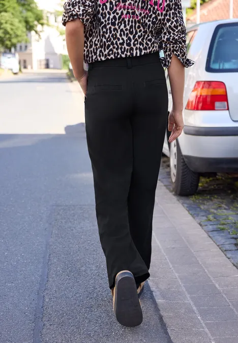 Une personne en pantalon noir et chemisier léopard marche sur le trottoir à côté de voitures garées.