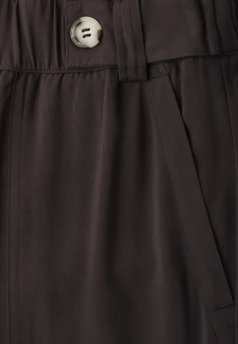 Gros plan d’un pantalon sombre avec taille élastique, poche latérale et bouton clair.