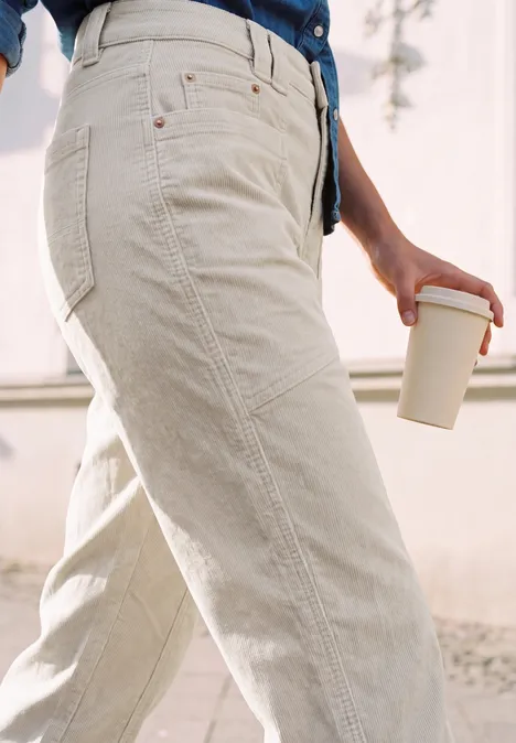 Personne porte un pantalon en velours clair et tient un gobelet à emporter