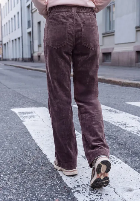 Personne vue de dos traverse un passage piéton en pantalon en velours côtelé marron et baskets blanches.