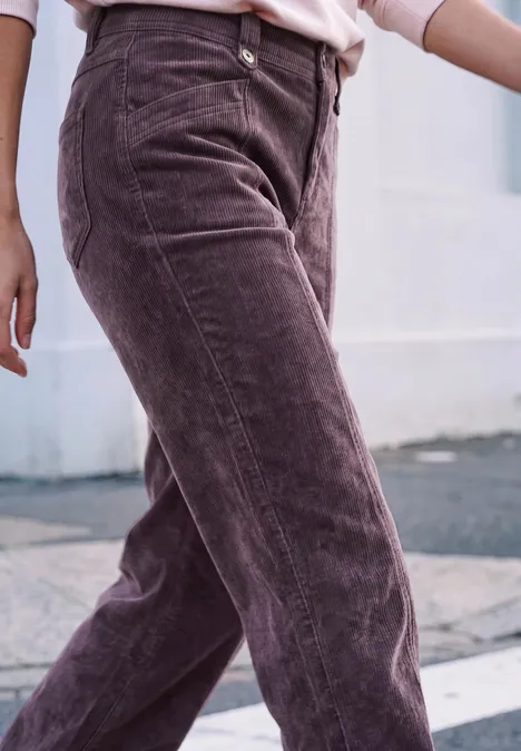 Gros plan sur une personne en pantalon en velours côtelé violet, debout sur un trottoir.