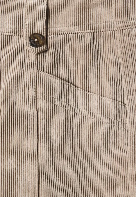 Gros plan d’un pantalon en velours côtelé beige à fines rayures, poche avant et bouton visibles
