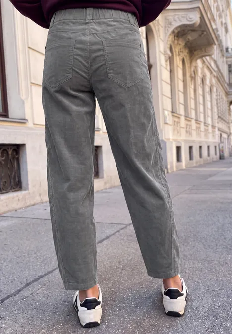 Person mit grauen Cordhosen und weißen Sneakers auf städtischem Gehweg.