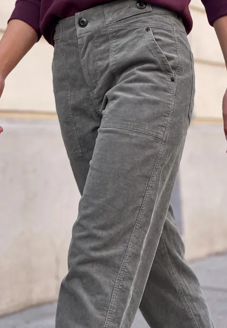 Graue Cordhose in lässigem Schnitt, getragen von Person mit dunklem Oberteil, vor urbanem Hintergrund.