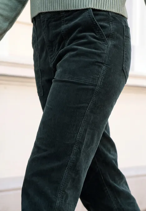 Eine Person trägt dunkelgrüne Cordhose, Beine gekreuzt, unteres Körperteil im Fokus.