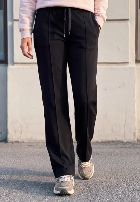 Mid Waist Broek met Wide Leg pijpen in casual pasvorm Black Iemand draagt een zwarte, recht gesneden broek en sneakers, staand voor een muur.