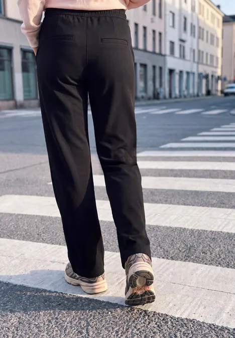 Mid Waist Broek met Wide Leg pijpen in casual pasvorm Black Persoon in zwarte joggingbroek en sneakers loopt over een zebrapad in stedelijke omgeving.