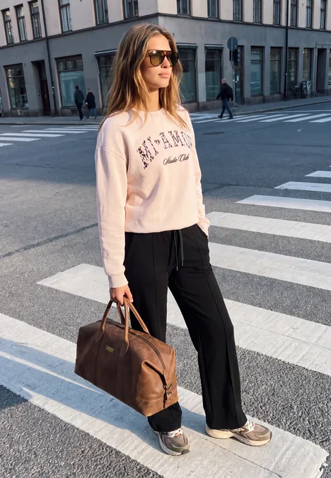 Mid Waist Broek met Wide Leg pijpen in casual pasvorm Black Vrouw met zonnebril loopt ontspannen over zebrapad in de stad, bruin reistas tas bij zich.