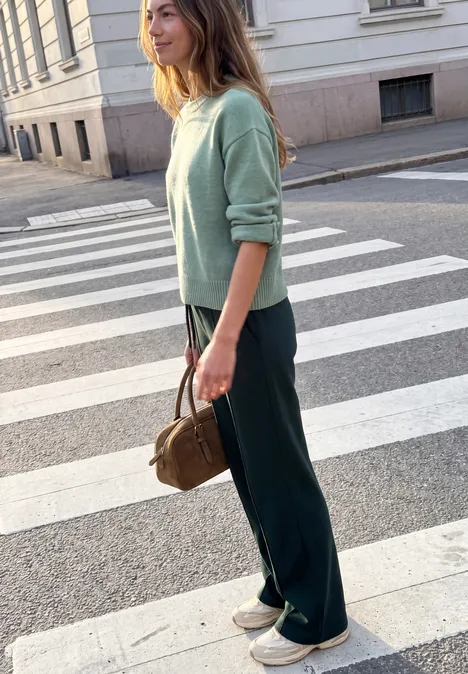 Mid Waist Broek met Wide Leg pijpen in casual pasvorm velvet pine Vrouw in mintgroene trui, donkere broek en witte sneakers met bruine tas, wachtend bij een zebrapad.