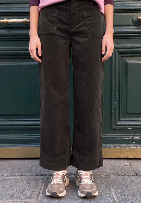 Schwarze, weite Cordhose mit umgeschlagenem Saum und Sneakers, Person steht vor einer grünen Tür auf dem Gehweg.