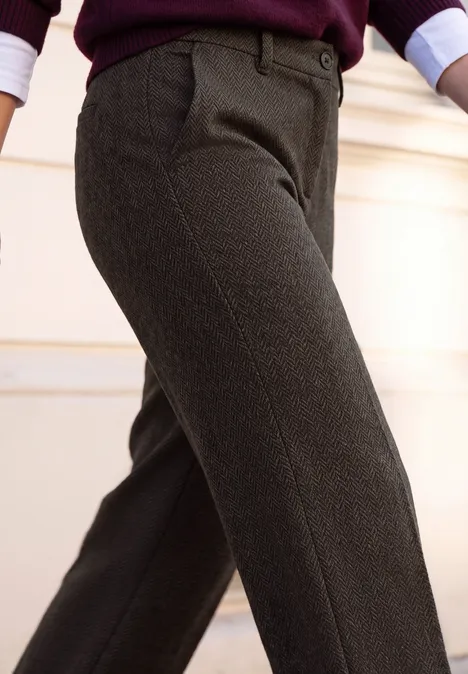 Plan rapproché d'une personne portant un pantalon en tissu gris foncé avec ceinture, un pull bordeaux et manches retroussées.
