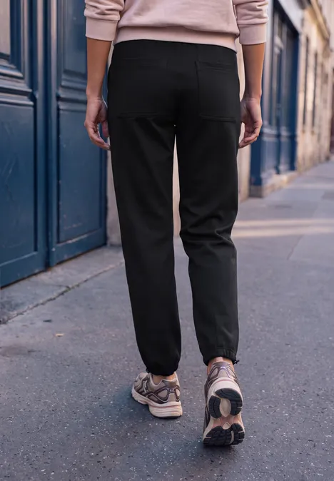 Person in schwarzen Hosen und Sneakers, von hinten auf einem Gehweg einer Stadt Straße, moderner Casual-Look.