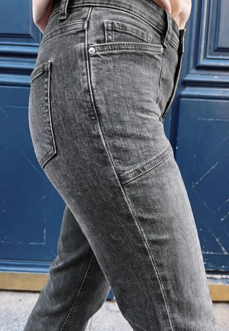 Person trägt graue Jeans, seitlich vor einer blauen Tür fotografiert.