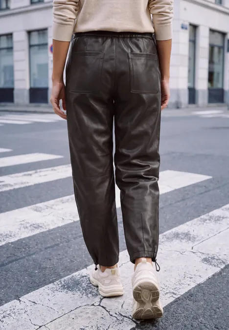 Eine Person geht über einen Zebrastreifen, trägt eine schwarze Lederhose und weiße Sneaker.