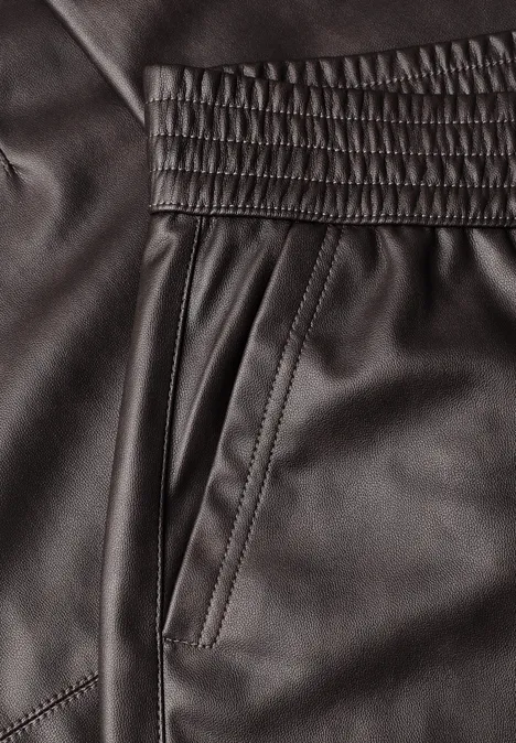 Detailaufnahme schwarzer Lederhose mit Gummibund, seitlicher Tasche und Ziernähten.