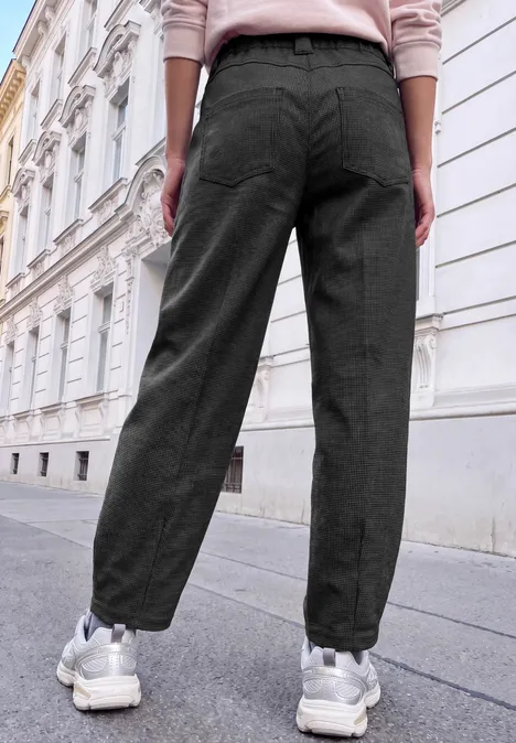 Eine Person steht in schwarzen Stoffhosen und weißen Sneakern vor einer historischen Hausfassade.