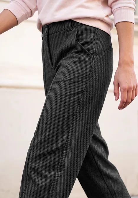 Damenmodell trägt elegante dunkelgraue Stoffhose mit Bundfalten und seitlichen Eingrifftaschen, kombiniert mit rosa Pullover.