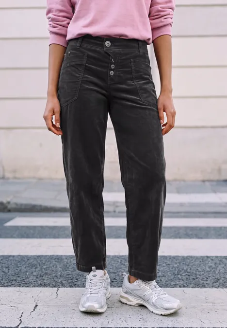 Persoon staat op stoep met zwarte corduroy broek en witte sneakers