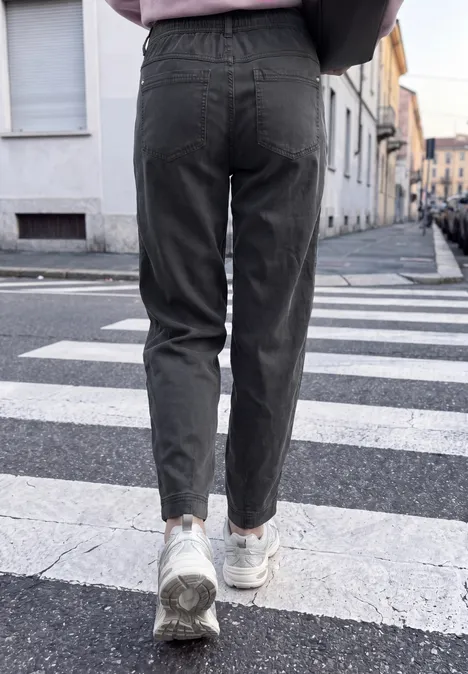 Person in dunklen Jeans und weißen Sneakers geht über einen Zebrastreifen in städtischer Umgebung.
