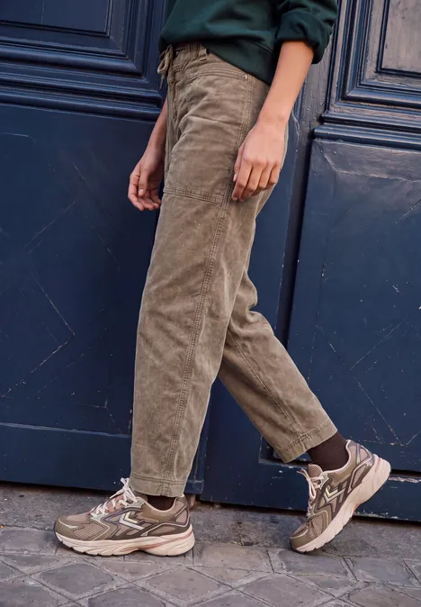 Mid Waist Barrel Leg Hose im Loose Fit henna brown Eine Person trägt beige Cordhosen und braune Sneaker vor einer dunklen Tür