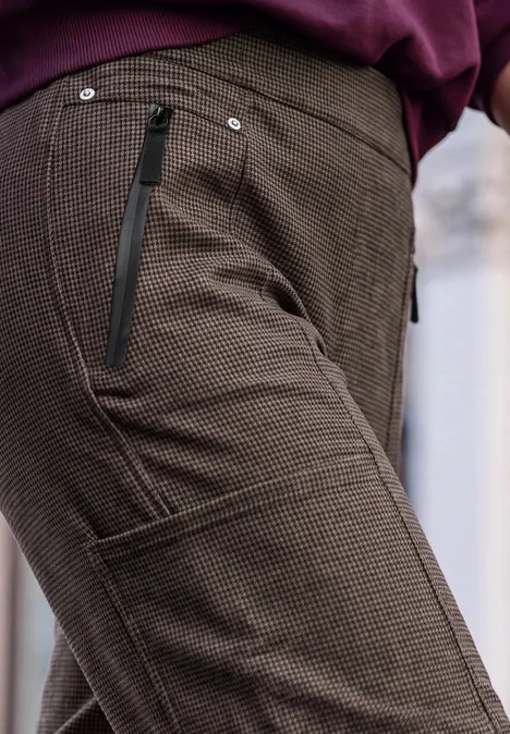 Nahaufnahme einer braunen Textilhose mit Reißverschlusstaschen und aufgesetzter Beintasche.