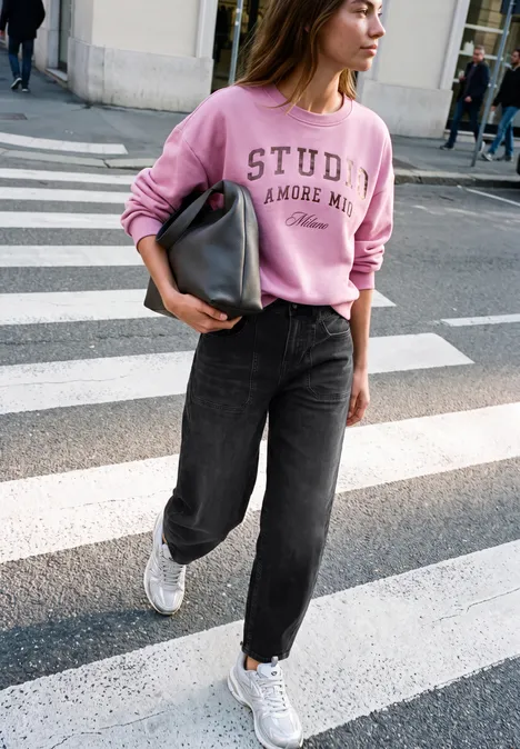 Relaxed Barrel Leg Leg Jeans im Loose Fit soft black washed Eine Frau in rosa Sweatshirt und schwarzen Jeans geht zu Fuß über einen Zebrastreifen, trägt weiße Sneaker.