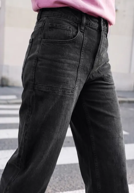 Relaxed Barrel Leg Leg Jeans im Loose Fit soft black washed Nahaufnahme einer Person in weiten schwarzen Jeans und rosa Oberteil beim Überqueren einer Straße.