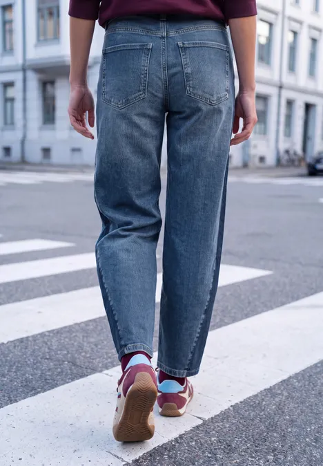 Relaxed Barrel Leg Leg Jeans im Loose Fit mid blue washed Person in blauen Jeans und bunten Sneakern geht über einen Zebrastreifen in urbaner Umgebung.