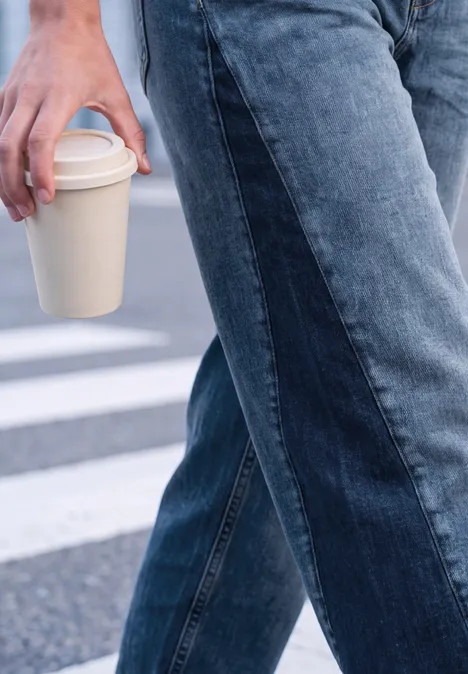 Relaxed Barrel Leg Leg Jeans im Loose Fit mid blue washed Person in Jeans hält einen Coffee-to-go-Becher und geht über einen Zebrastreifen.