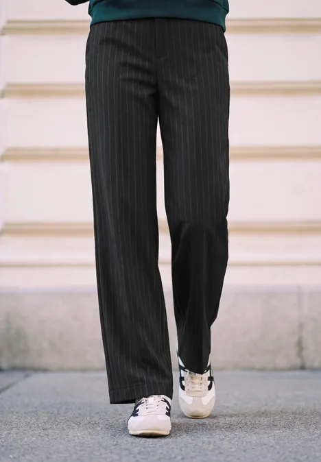 High Waist Straight Leg Hose im Casual Fit Black Eine Person trägt schwarze Nadelstreifenhose und weiße Sneaker auf Gehweg.
