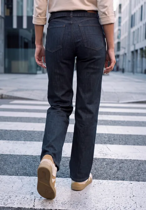 Vue de dos d'une personne en jean et baskets beiges traversant un passage piéton en ville.