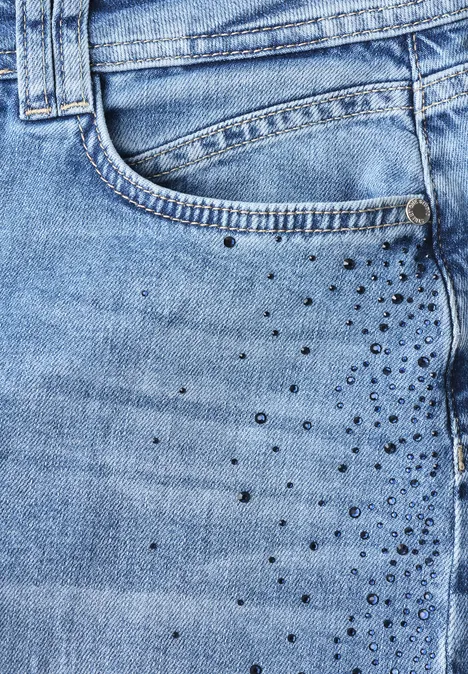 Close-up van een lichtblauwe spijkerbroek met voorzak en kleine metalen studs als versiering.