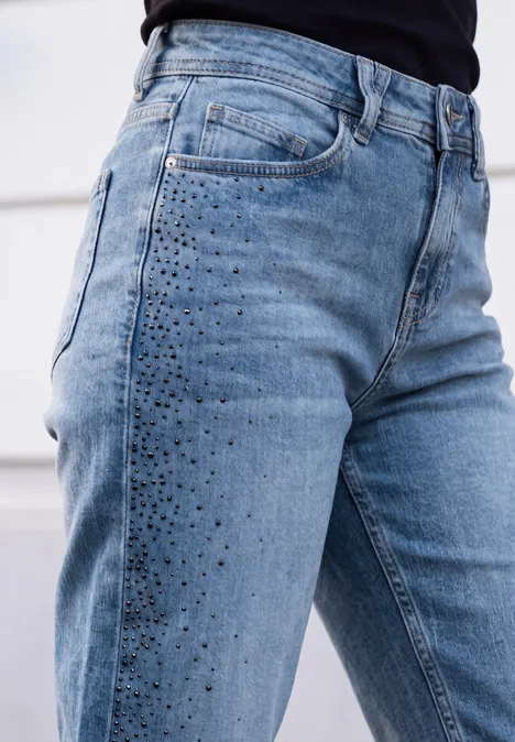 Close-up van een lichtblauwe high-waist jeans met glinsterende studs op het bovenbeen.