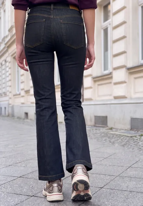 Persoon in donkere wijde jeans en sneakers loopt op een stoep langs een klassieke gevel.