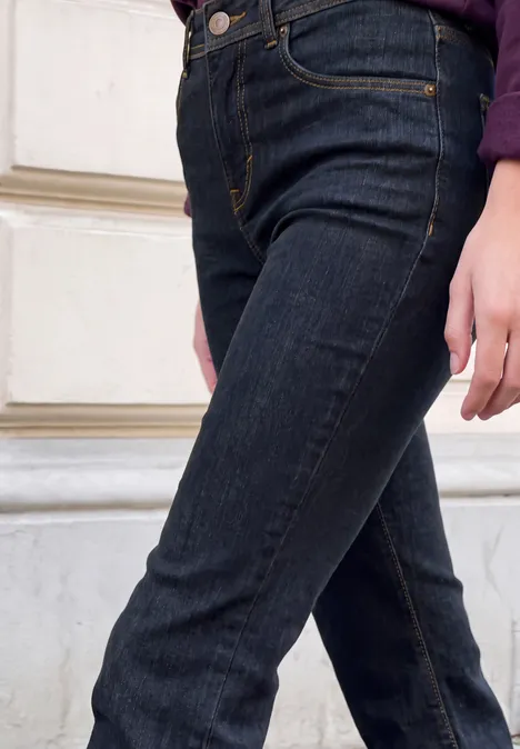 Donkere high-waist jeans, nauwsluitende pasvorm, persoon staat zijwaarts, hand ontspannen langs het bovenbeen.