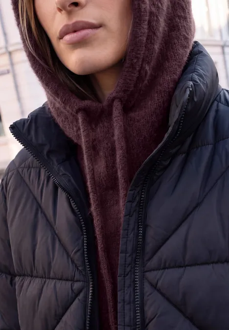 Nahaufnahme einer Person mit kastanienbraunem Kapuzenpullover unter einer schwarzen Steppjacke.