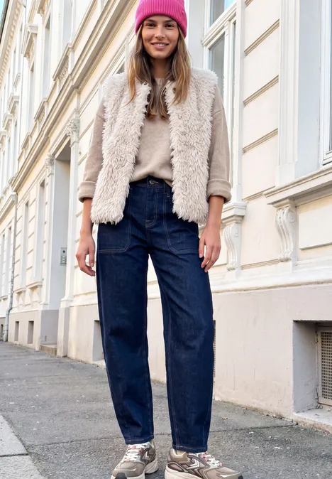 Strick-Beanie in Unifarbe ruby raspberry Junge Frau in pinkem Beanie, flauschiger Jacke und Jeans steht lächelnd an einer Hausfassade.