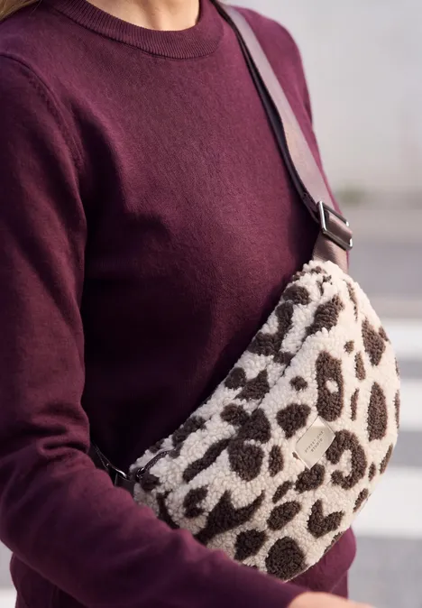 Eine Person trägt einen burgunderroten Pullover und eine Crossbody-Tasche mit Leopardenmuster.