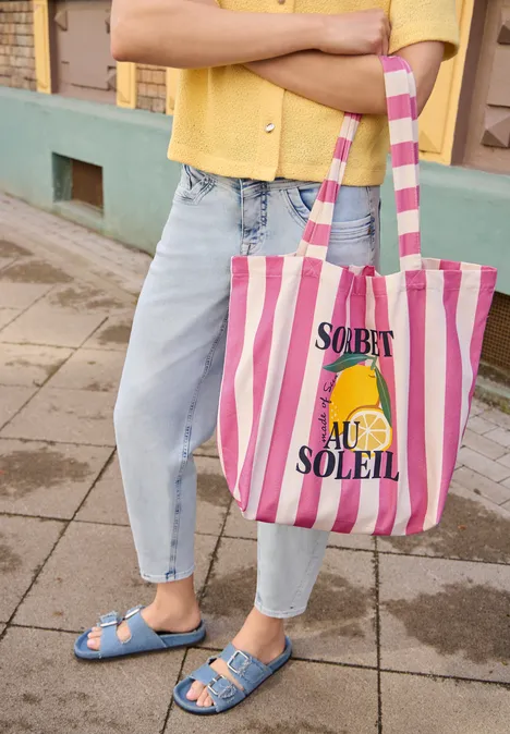 Canvas Shopper mit Streifenmuster multicolor Person in Jeans und blauen Sandalen hält gestreifte Tasche mit Zitronengrafik und „Sorbet au Soleil“-Aufdruck.