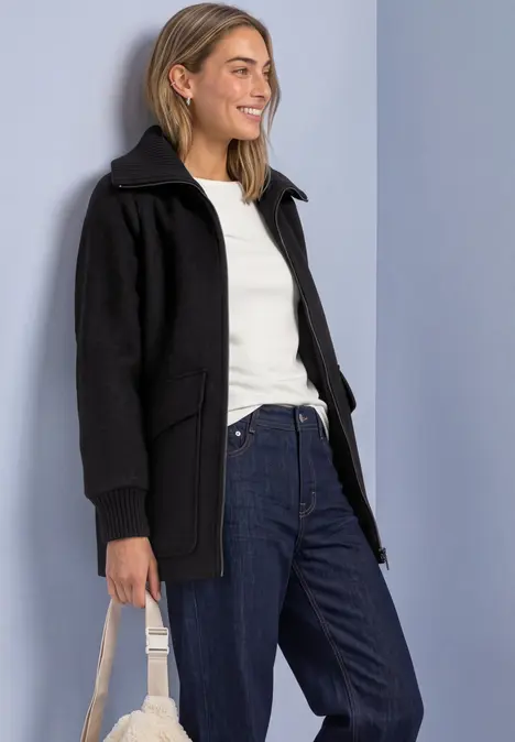 Femme en veste à capuche noire, t-shirt blanc, jean et sac beige.